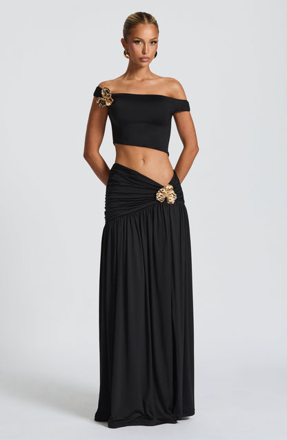 Conjunto negro de frente: top corto con hombros caídos y falda larga fruncida con broche.