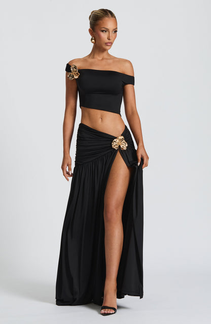 Conjunto negro de top fuera de hombros y falda larga con abertura lateral; broche dorado.